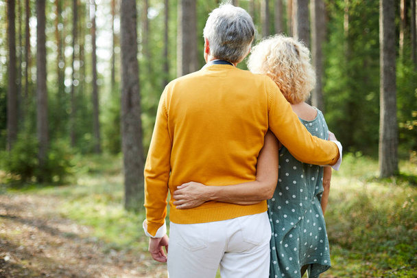 Blick zurück auf umarmende Senioren in Freizeitkleidung, die an einem Sommertag im Wald chillen - Foto, Bild
