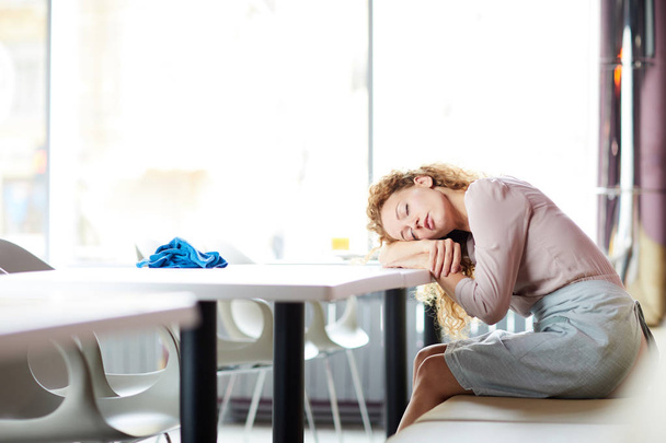 Müde junge Kellnerin schläft mitten im harten Arbeitstag auf dem Tisch - Foto, Bild