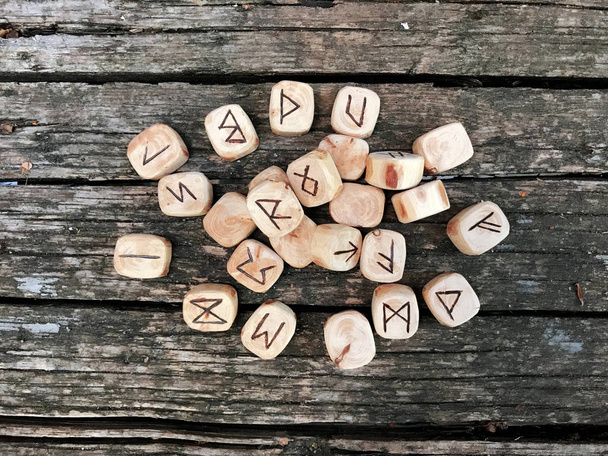 A stack of wooden runes at forest. Wooden runes lie on a old wood background. Runes are cut from wooden blocks. On each rune symbol for fortune telling is designated. - Foto, Imagen