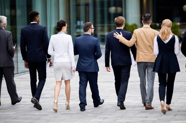 Vista trasera de los empleados elegantes en trajes que bajan por el bulevar en la ciudad moderna
 - Foto, Imagen