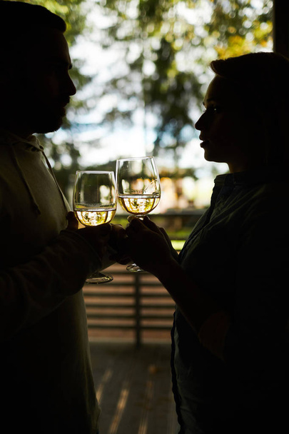 Silhouette felismerhetetlen szerelmi pár csengő pohár fehér bort, és nézi egymást szeretettel állva terasz - Fotó, kép