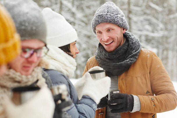Allegro giovani amici in cappotti caldi parlando tra loro e bevendo tè dalla tazza thermos in escursione invernale
 - Foto, immagini