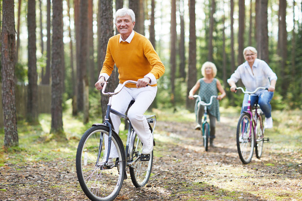 Веселые возбужденные старшие друзья в повседневной одежде наслаждаясь активной жизнью на велосипедах вместе в лесу, они мчатся друг к другу
 - Фото, изображение