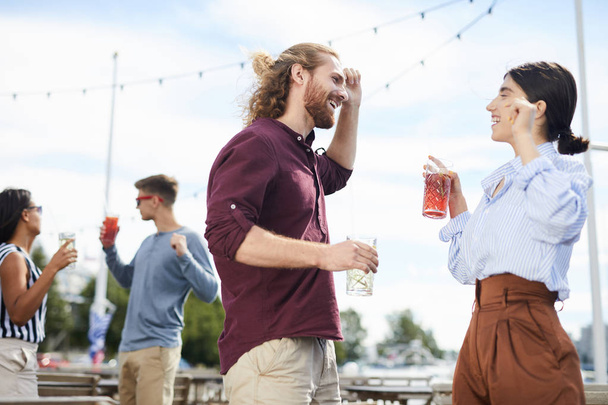 Nuori ekstaattinen pari juomien kanssa nauttien tanssia ja puhua ulkona
 - Valokuva, kuva