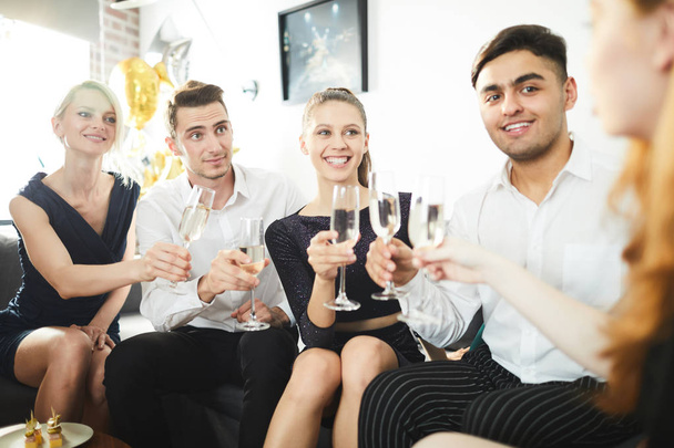 Dois jovens casais em roupas inteligentes animando-se com champanhe enquanto desfruta de festa em casa
 - Foto, Imagem