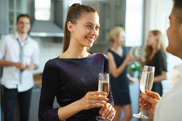 Усміхнена гламурна дівчина з шампанським розмовляє з хлопцем, насолоджуючись домашньою вечіркою
 - Фото, зображення