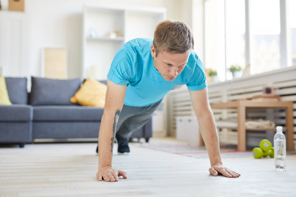 Fiatal aktív férfi fekvőtámaszozik reggel, miközben otthon marad. - Fotó, kép