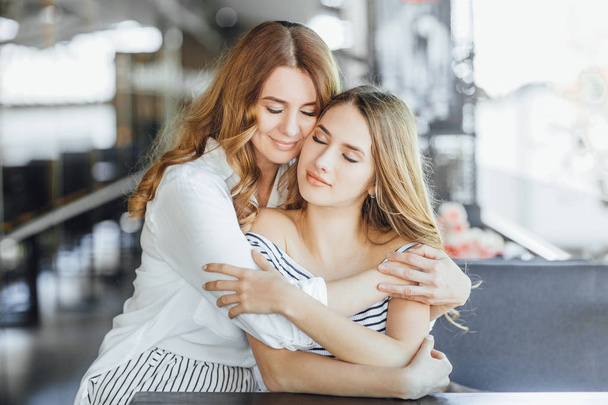 Mom and young daughter hugging on summer terrace in casual clothing, selective focus - Фото, изображение