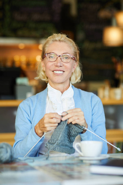 Mulher feliz olhando para a câmera enquanto tricô lenço quente ou suéter para o inverno
 - Foto, Imagem