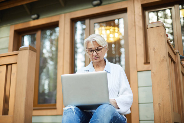 Poważne, Starsza kobieta z laptopa siedząc na tarasie i wyszukiwanie danych w necie - Zdjęcie, obraz