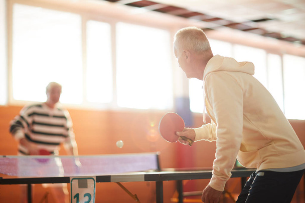 L'un des hommes actifs frappant balle de ping-pong sur la table tout en appréciant le jeu avec son ami dans le sport ou centre de loisirs
 - Photo, image