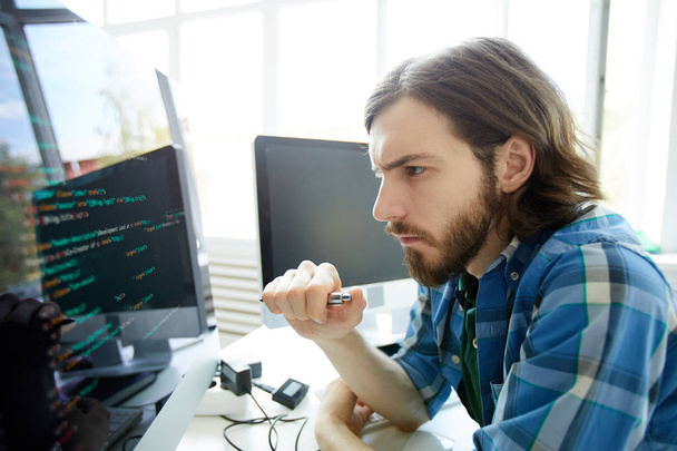 Konzentrierter junger Softwareentwickler blickt auf Datencode auf Computerbildschirm - Foto, Bild