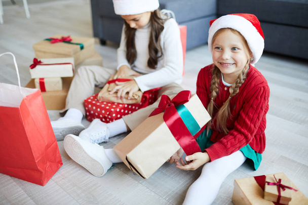 Joyeux petit Père Noël mignon avec grande boîte-cadeau assis sur le sol avec sa sœur près de chez
 - Photo, image