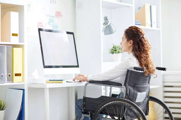 Современная деловая женщина сидит в инвалидной коляске перед компьютером, печатает и просматривает в сети
 - Фото, изображение