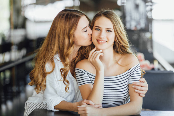 Mom kissing daughter on summer terrace in casual clothing - Foto, Imagen