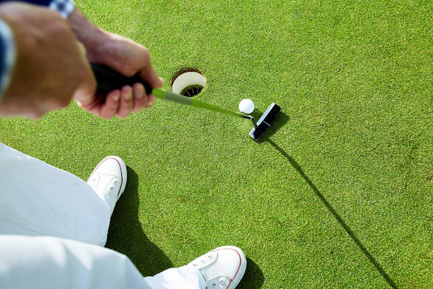 Aktiver Mann steht auf grünem Rasen am Golfloch mit Schläger nah am Ball vor dem Schlag - Foto, Bild
