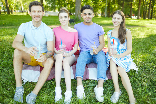 Glückliche junge Begleiter versammelten sich zum Picknick auf grünem Rasen im Freizeitpark - Foto, Bild