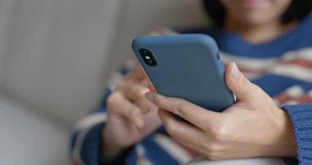 Жінка використовує мобільний телефон і сидить на дивані вдома
 - Фото, зображення