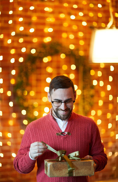 Joyeux homme d'affaires déliant ruban d'or sur le dessus de la boîte-cadeau pendant la fête de Noël au bureau
 - Photo, image
