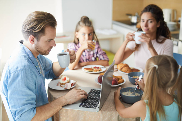 Młody mężczyzna szuka czegoś w sieci podczas śniadania z żoną i córeczkami - Zdjęcie, obraz