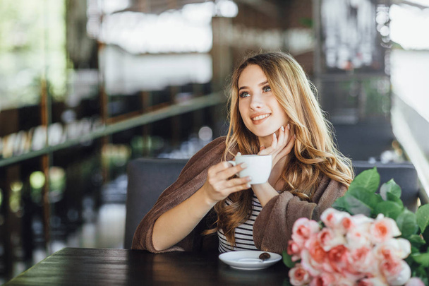 Young woman in casual clothes resting and drinking coffee on summer terrace  - Foto, Bild