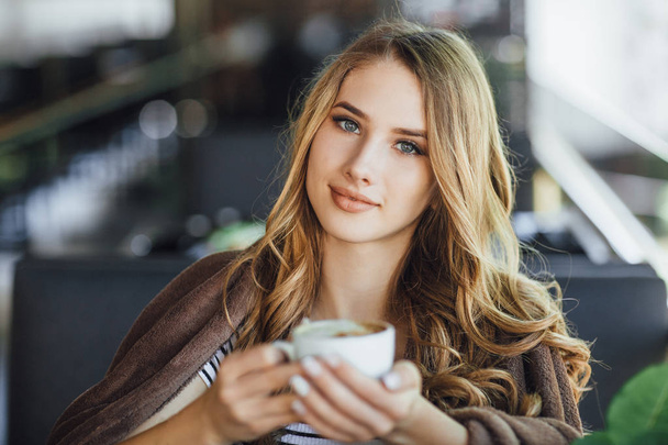 Young pretty woman in casual clothes resting and drinking coffee on summer terrace  - Foto, afbeelding
