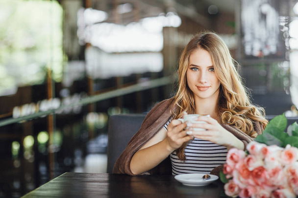 Young woman in casual clothes resting and drinking coffee on summer terrace - Фото, изображение