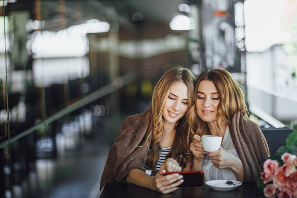 woman with daughter using smartphone and drinking coffee at cafe - Foto, Bild