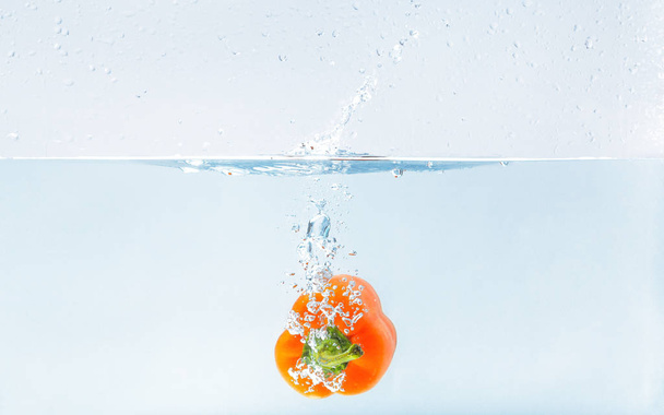 Värilliset oranssi paprika veteen roiskeet sinisellä pohjalla
 - Valokuva, kuva