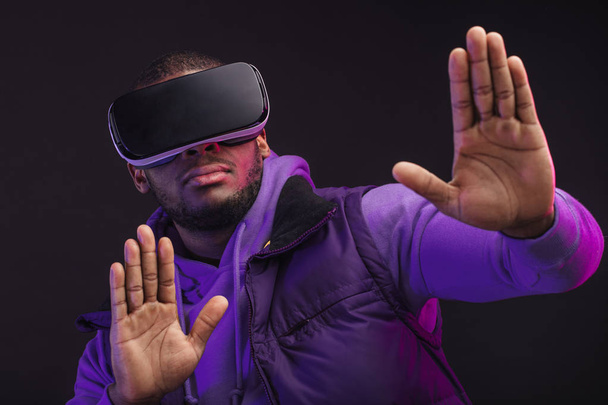 African man wearing virtual reality goggles isolated on dark purple background - Фото, изображение