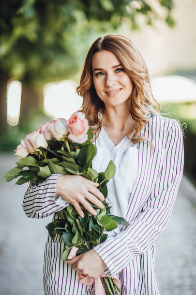 Portrait of blonde woman in casual clothes in street with bouquet of roses - Fotoğraf, Görsel