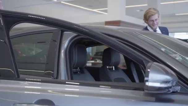 Happy couple just bought car in modern motor show. Man and woman open doors and sit inside big modern car, smiling. Concept of buying a vehicle. Car showroom. - Filmmaterial, Video
