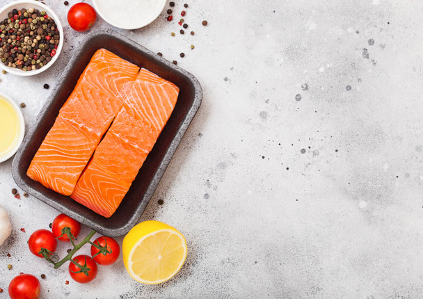 Plastic container with fresh salmon slice with oil tomatoes and lemon on stone kitchen background. Space for text - 写真・画像