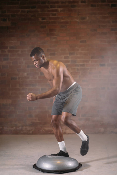African sportsman performing exercise on bosu ball in crossfit gym - 写真・画像