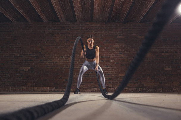 Jonge Kaukasische vrouw uit te werken met touwen van de slag bij een sportschool - Foto, afbeelding