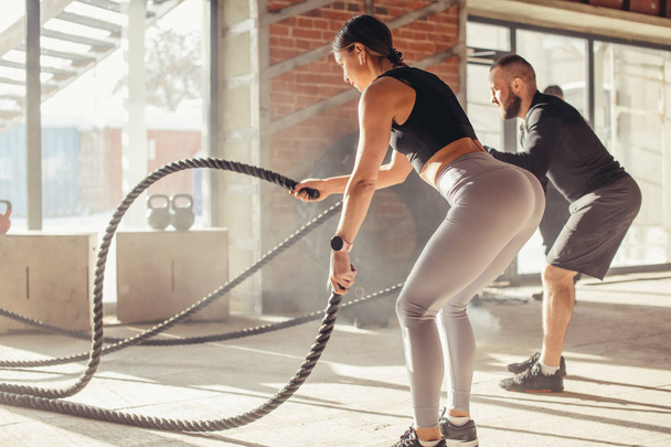 Woman and man in gym functional training with battle rope exercising - Foto, afbeelding