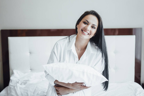 Portrait of beautiful woman in bed with pillow in arms - Φωτογραφία, εικόνα