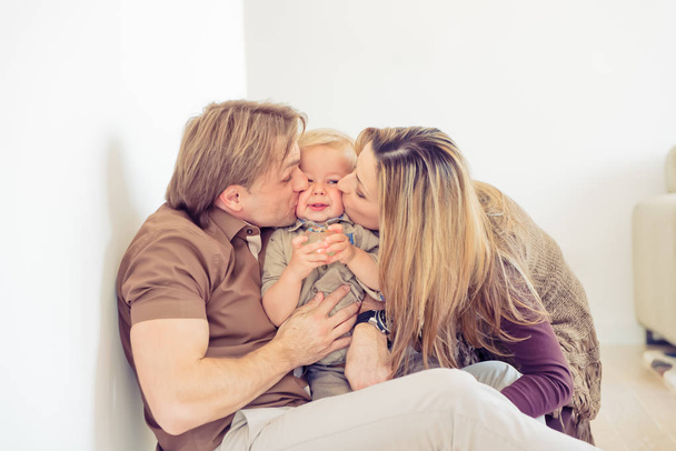 Šťastná rodina sedí na podlaze s jejich děťátko. Rodina trávila čas se svým synem. Rodiče líbat jejich dítě. - Fotografie, Obrázek