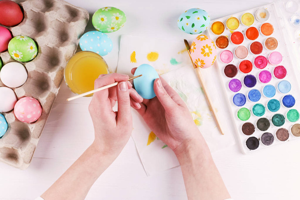 Hand painted Easter eggs, paints and brushes on a white table. Preparation for the holiday. Girls hands draw a pattern. - Foto, Imagen
