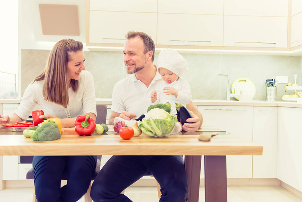 Parents heureux assis dans la cuisine et se prépare pour la cuisine avec leur bébé fille chef
. - Photo, image