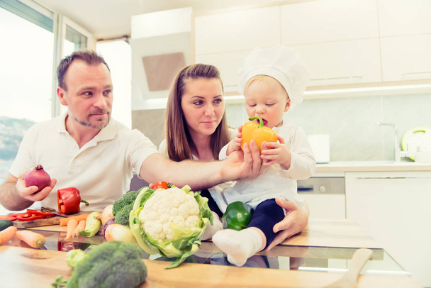Happy parents sitting in the kitchen and prepares for cooking with their baby girl chef. - Фото, зображення