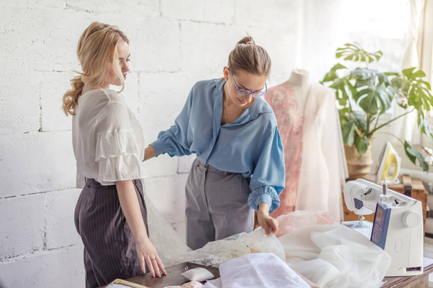 Professional female dressmaker choosing fabric together with attractive woman - Foto, imagen