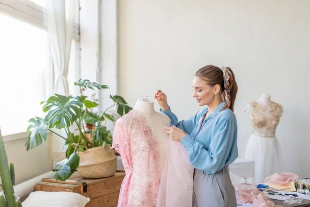 Beautiful seamstress is working with a wedding dress model in her studio - Zdjęcie, obraz
