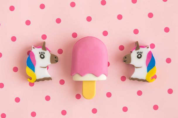 Flat lay of unicorns and ice cream on stick against rose background with polka dots. - Photo, image