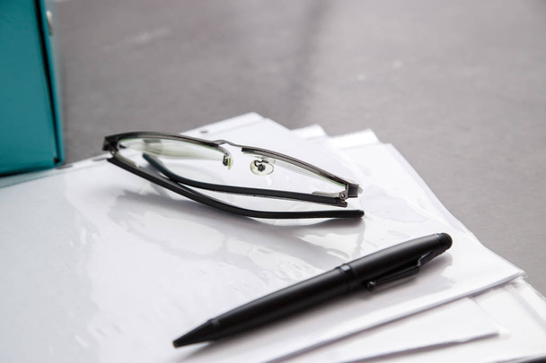 Black-rimmed optical glasses and black pen on documents on grey marble background - Zdjęcie, obraz