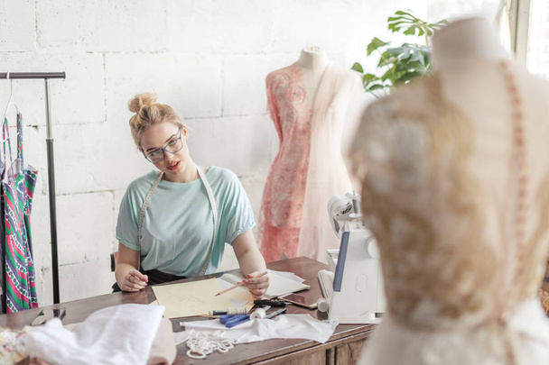 Fashion designer at work. Talanted dressmaker drawing sketch at her workspace - Фото, изображение