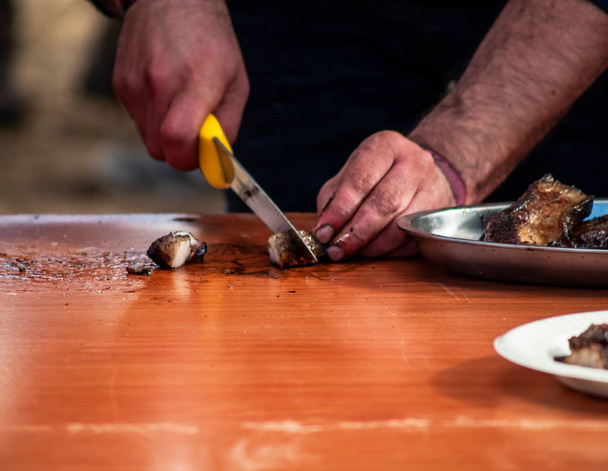 Onherkenbaar persoon vlees met een mes te snijden en het brengen van een papieren bord in de straat op een populaire feestje in een dorp in Spanje - Foto, afbeelding