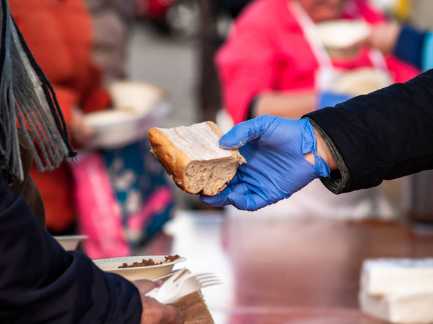 Een persoon met blauwe nitril handschoenen dienen een stuk brood - Foto, afbeelding