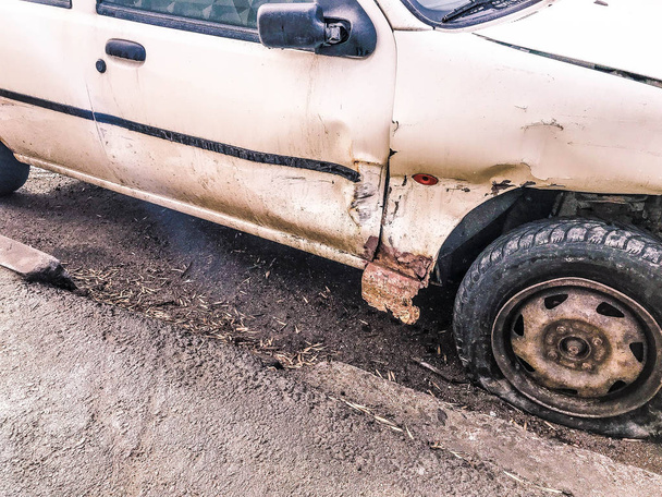 Viejo coche blanco oxidado roto de la carcasa con ruedas perforadas bajadas con arañazos corrosión y un parachoques roto con abolladuras y arañazos lanzados en la carretera. Basura automática
 - Foto, imagen