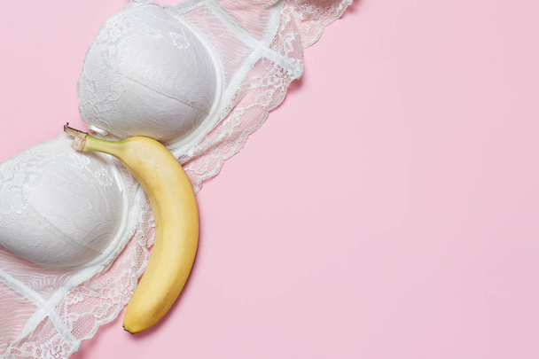 アダルト チャット, バーチャル セックスの概念。白のブラジャーとピンクの背景の大きなバナナ。ミニマルなフラット レイアウト平面図 - 写真・画像